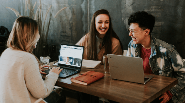 A group of smiling young people at their laptops and drinking coffee.