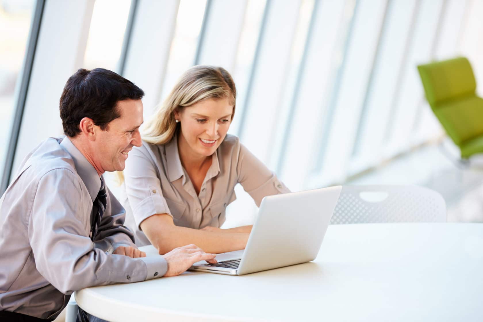 A woman and a man stare at one silver laptop.