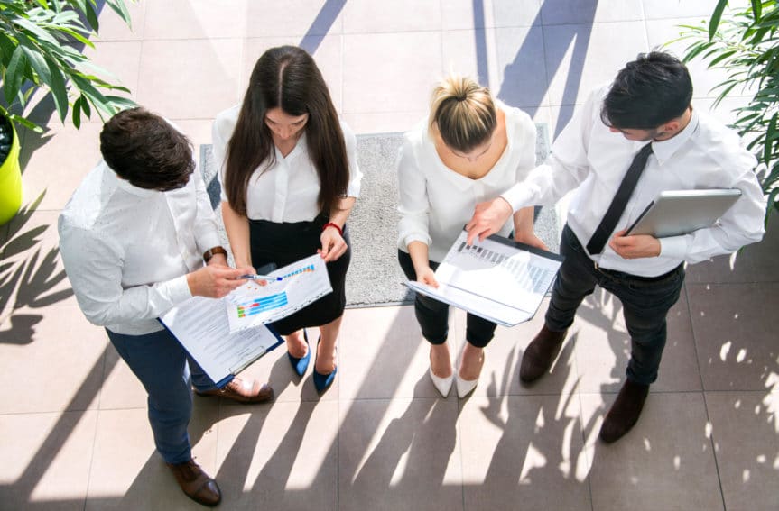A high angle image of four people in business clothes staring at sheets of paper.